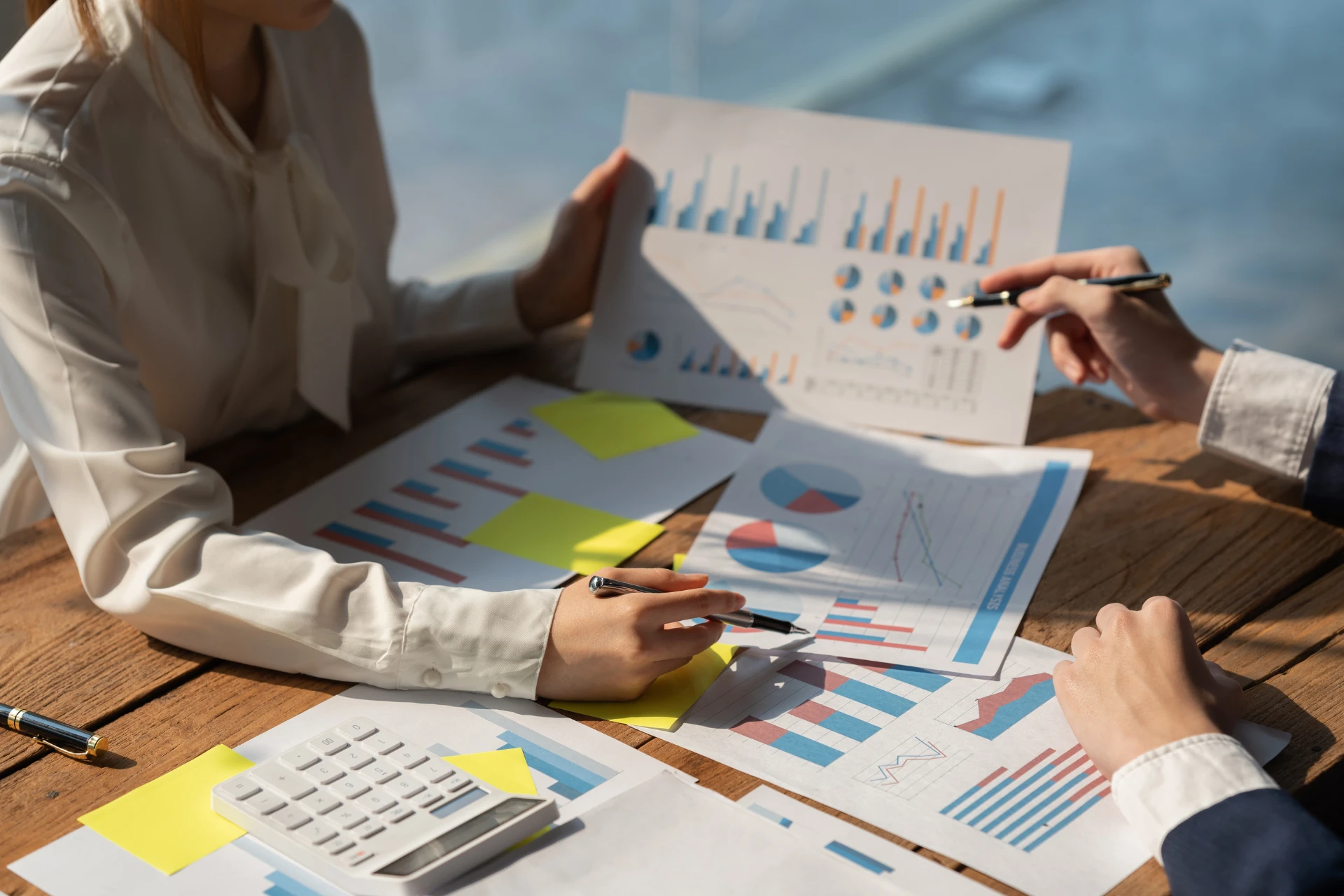 Two professionals sitting at a wooden table reviewing printed financial reports. 