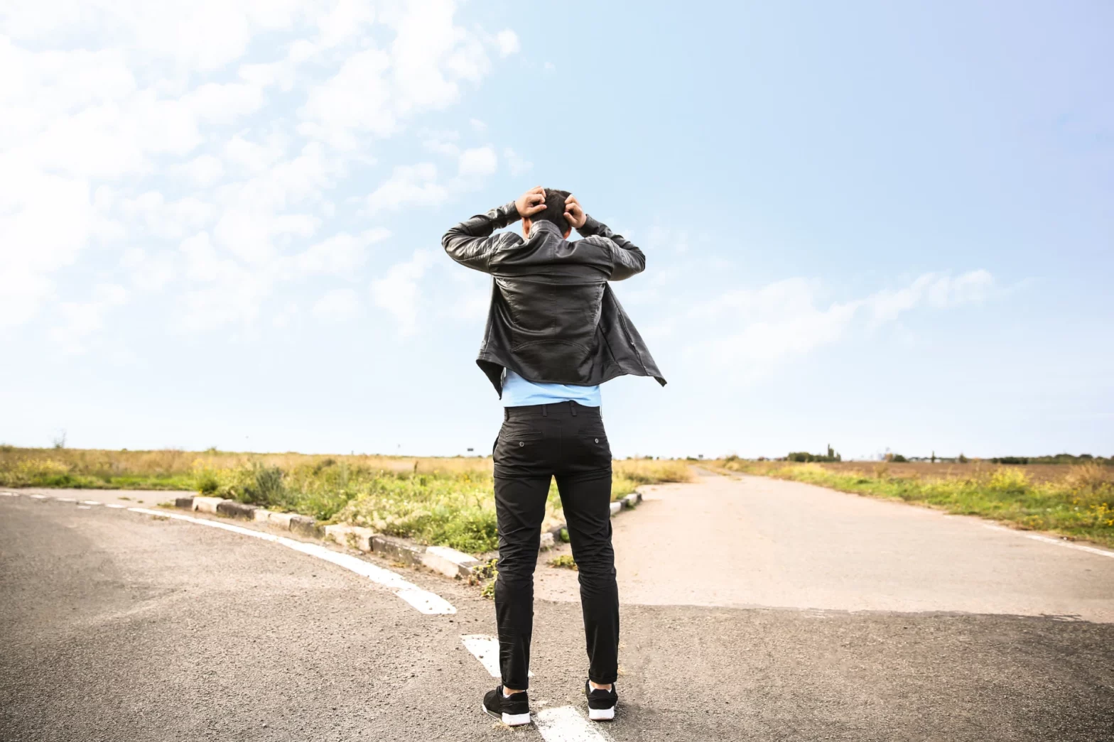 A man seen from behind holding his head in frustration at a fork in the road under a bright sky.