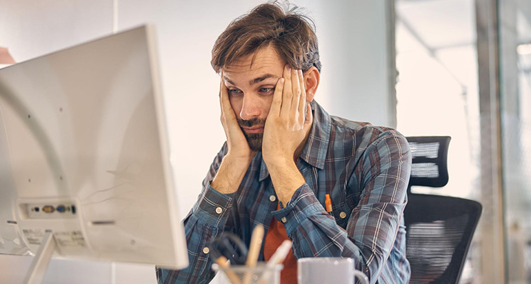 A stressed marketer holds his face with his hands as he stares at the computer screen
