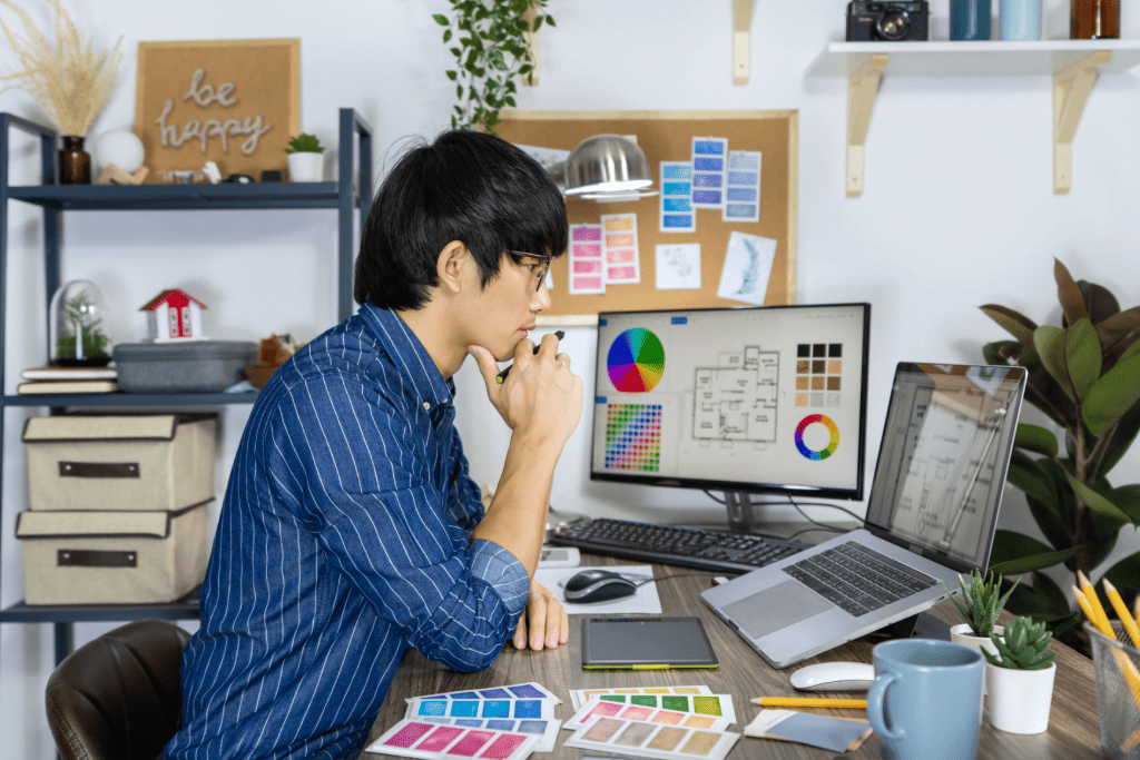 A graphic designer working at a computer surrounded by colour swatches 