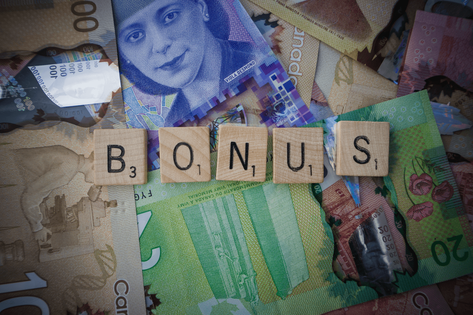 Scrabble tiles spelling out the word bonus on top of Canadian bills