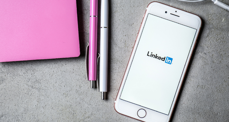 The LinkedIn logo displayed on a white smartphone beside two pens