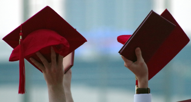 Two people holding up red graduation caps
