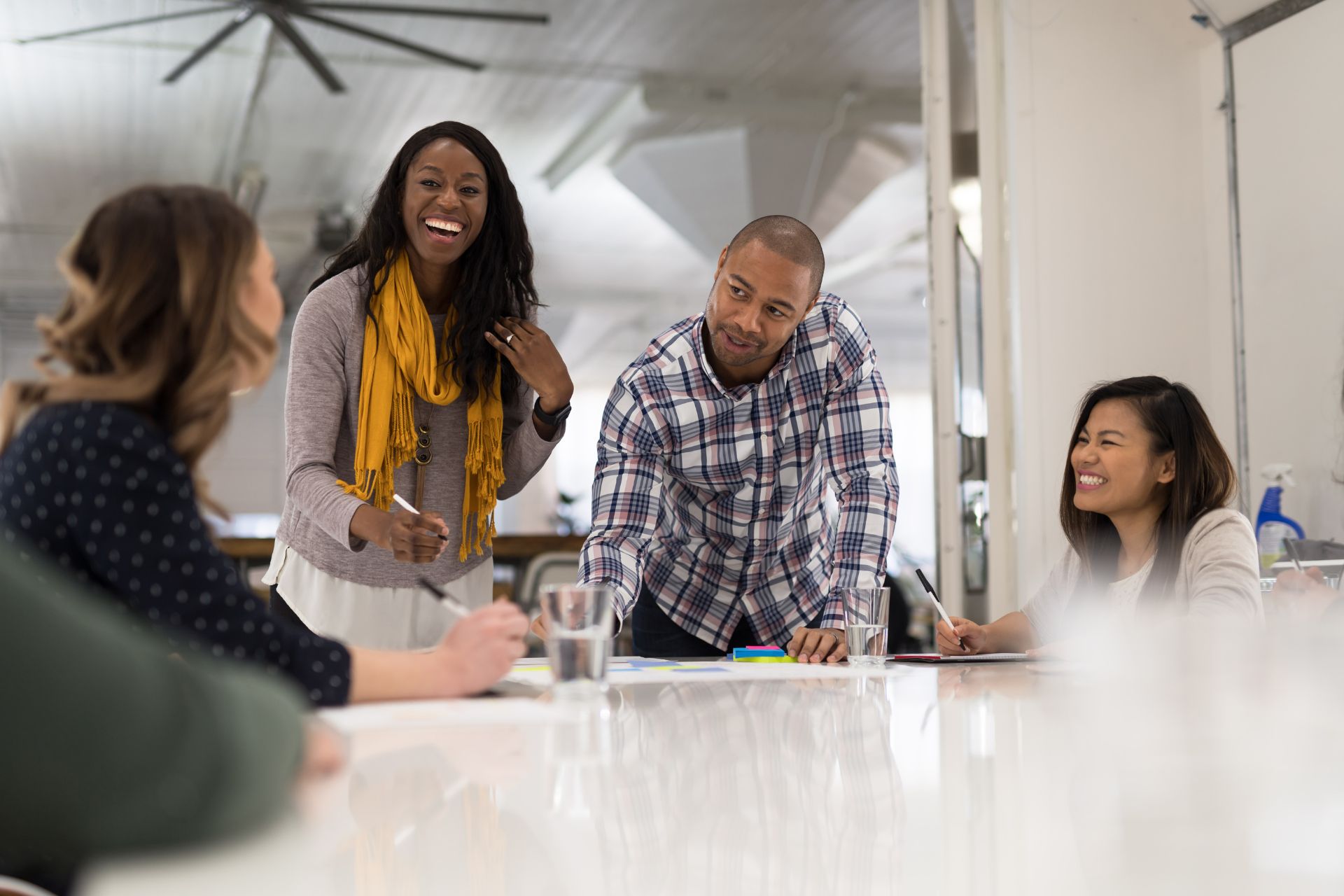 Four people from diverse ethnic backgrounds in an office, all smiling at each other while taking notes 