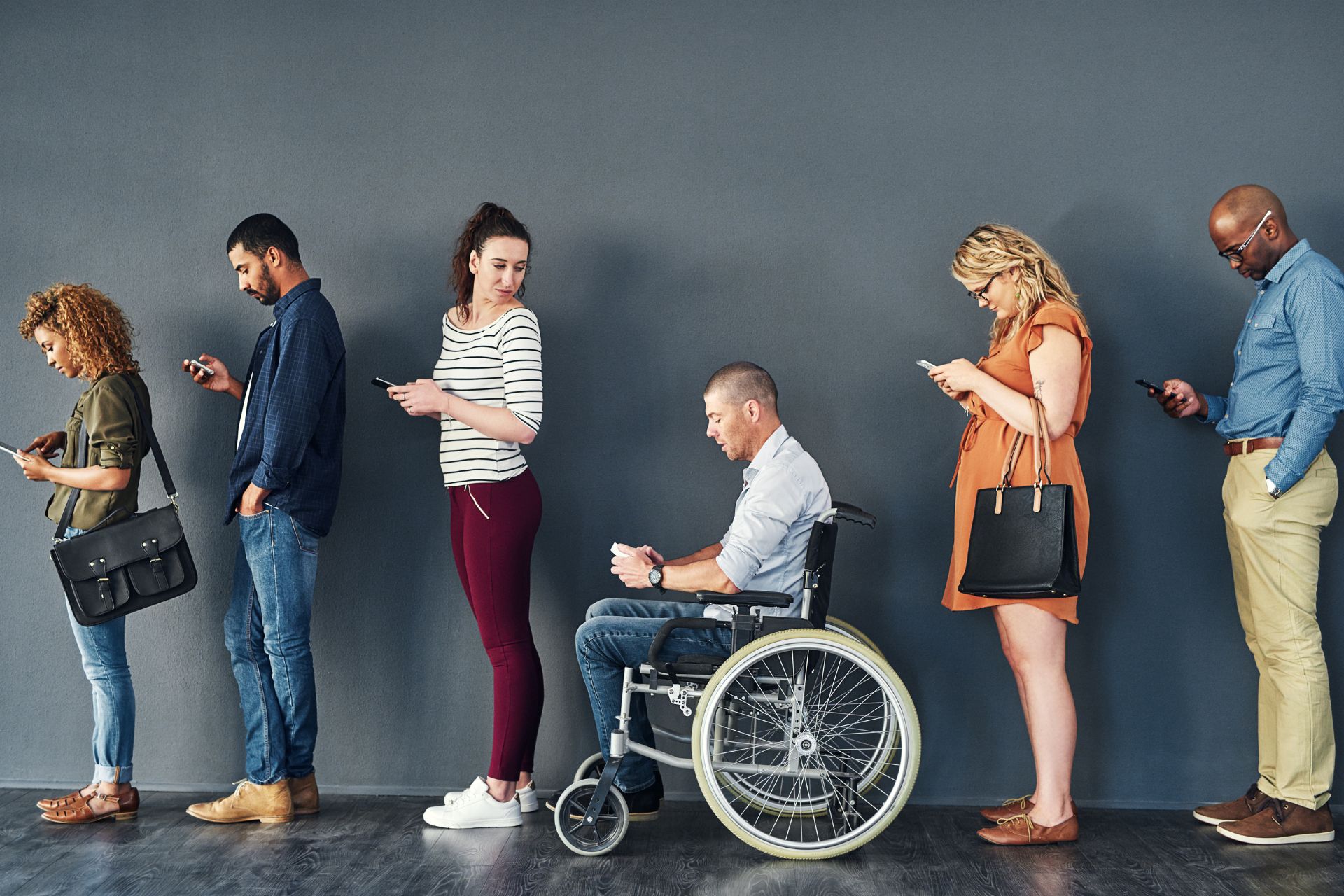 A group of people from diverse backgrounds standing in line against a gray background 