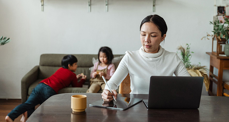 A mom working from home with her children playing behind her in the living room