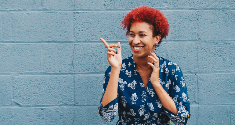 A smiling woman in a patterned blue shirt in front of a blue brick wall