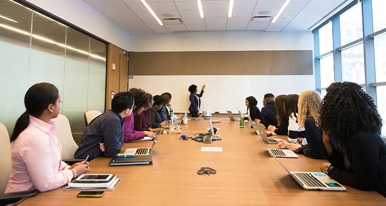 A group of people listening to a woman in a conference room