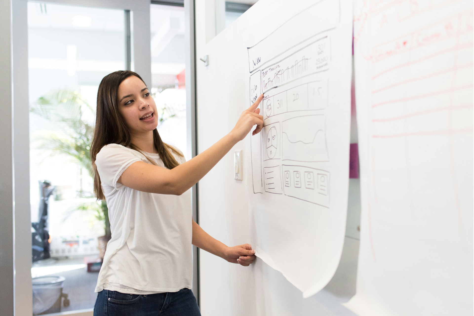 A woman in a white T-shirt doing a presentation and pointing at a white paper