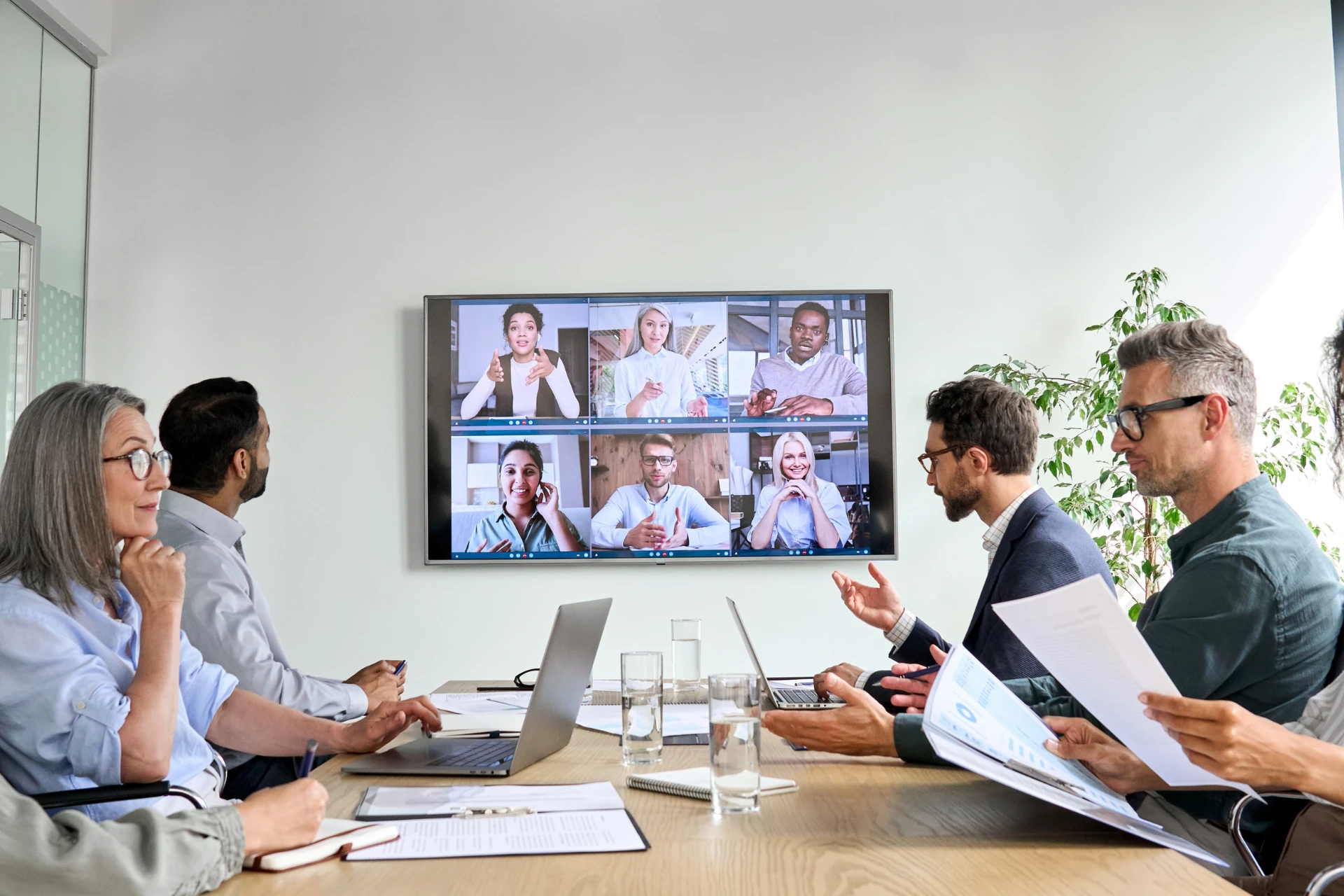 A diverse team having a meeting in-office with several employees tuned in on a virtual conference