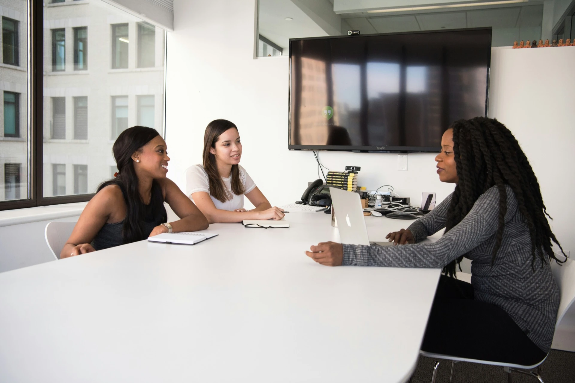 Three women sitting in an office with notebooks and a laptop 

