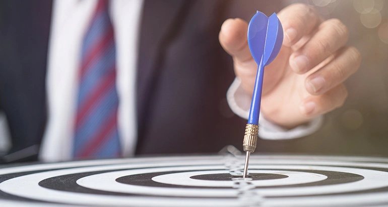 A business person places a dart on a bullseye, signifying he’s accomplished some career goals.