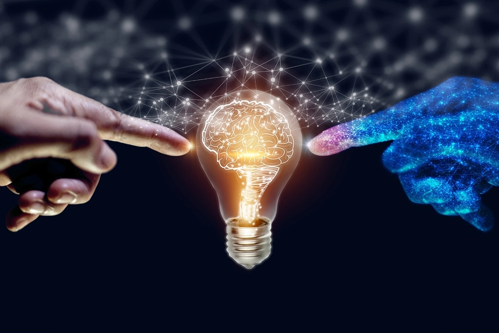 Human hand and AI-designed hand extend index fingers toward a central bulb with a brain, symbolizing the connection between humanity and artificial intelligence.