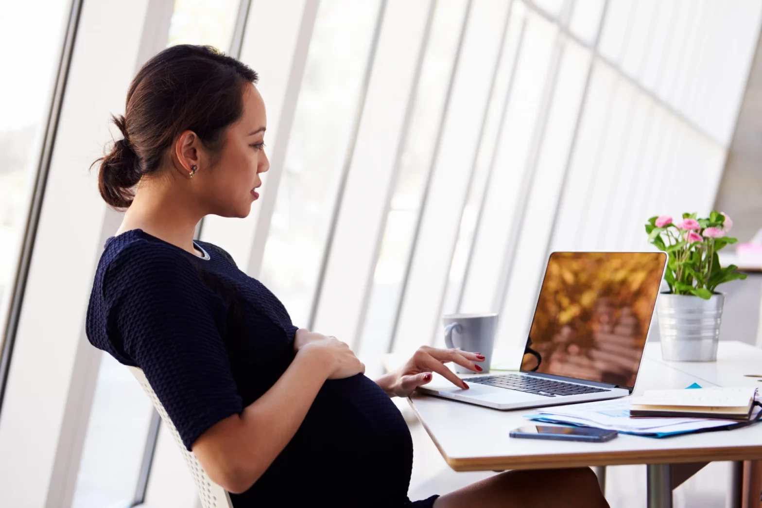 Pregnant business professional working on a laptop in a sunny office