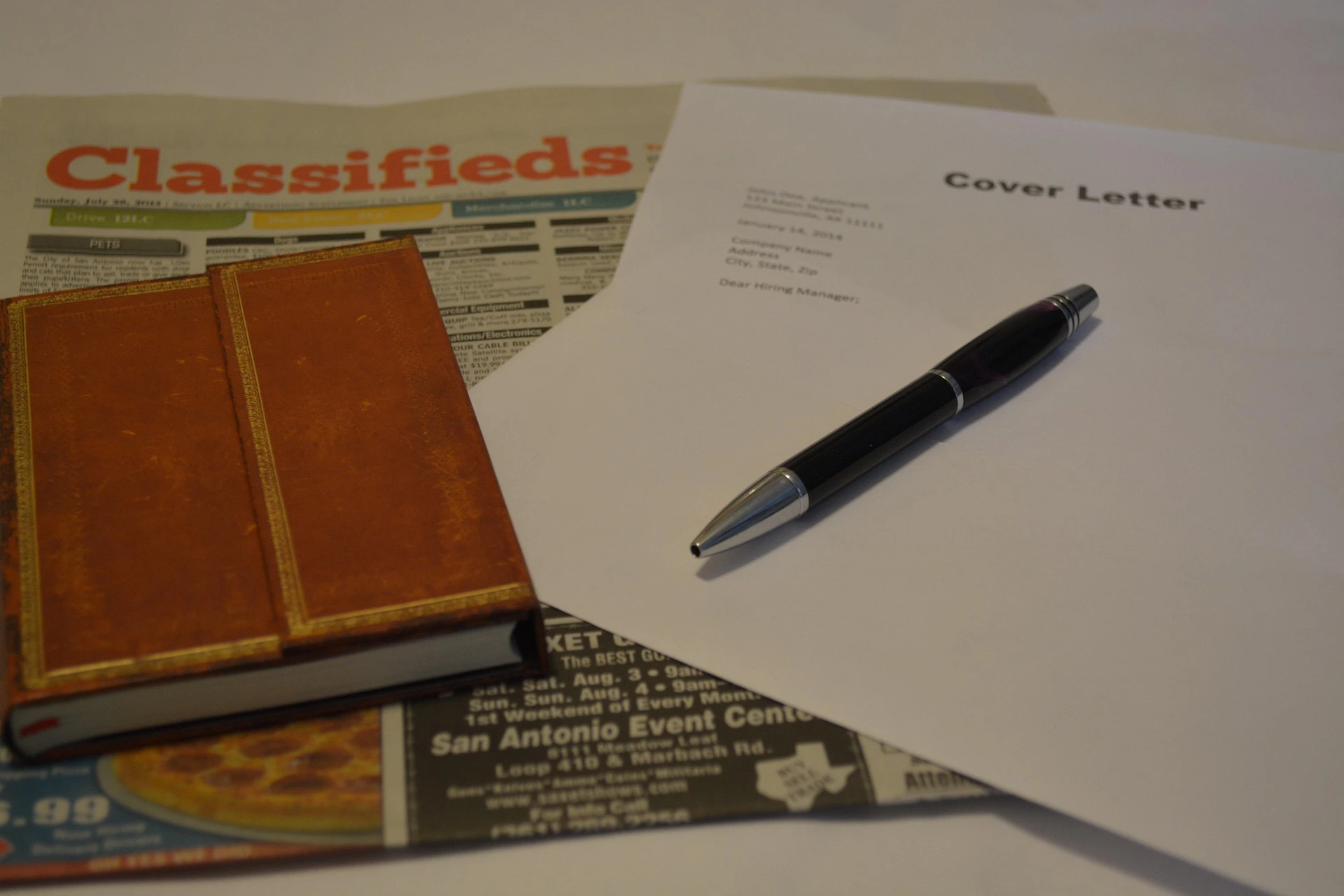 Classifieds newspaper beside brown notebook and pen 