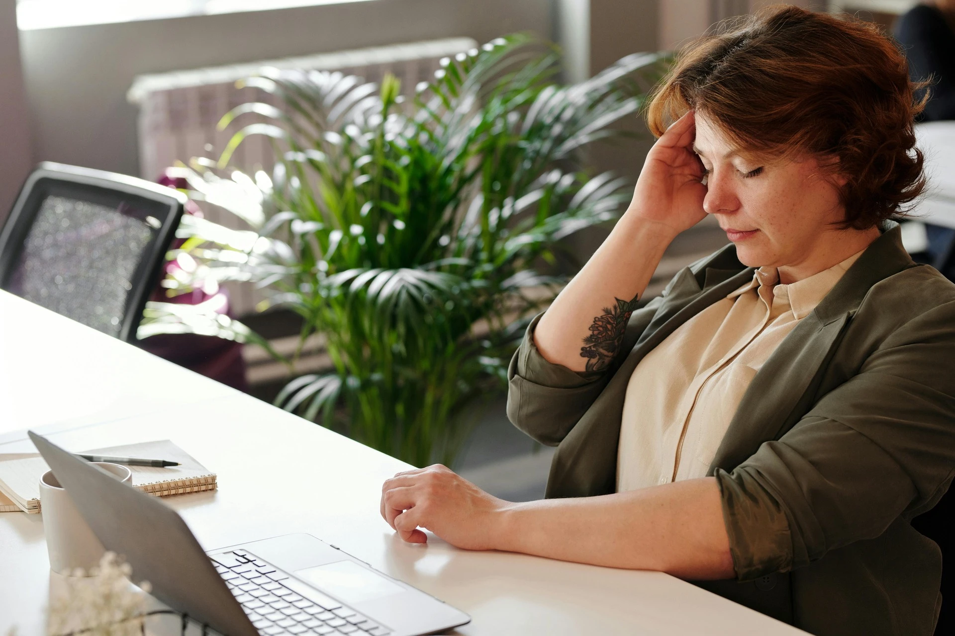 A woman holding her head at work sitting in front of a laptop